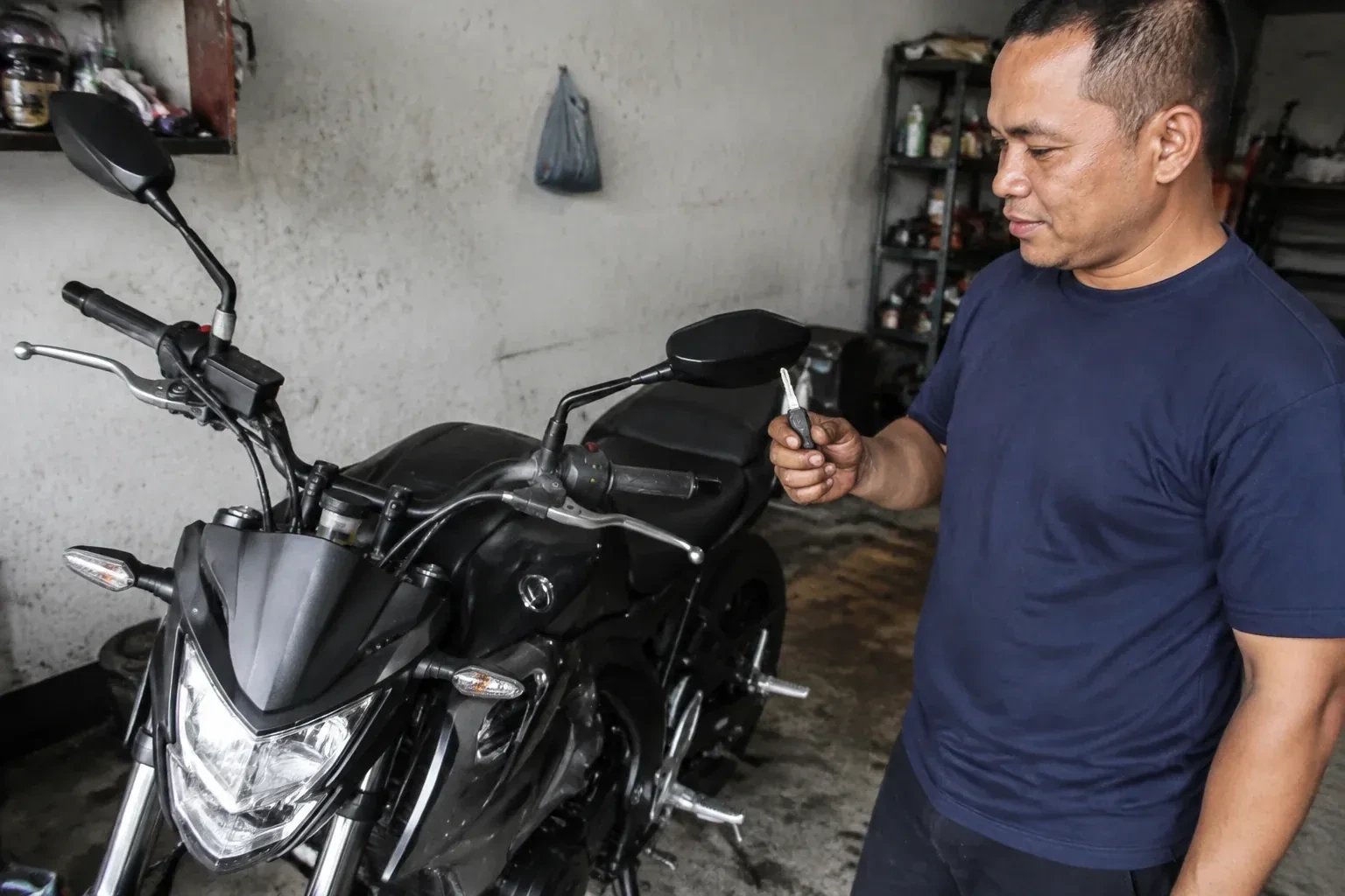 Person holding a key beside a black motorcycle in a garage. — Motorcycle & Scooter Keys, Toronto